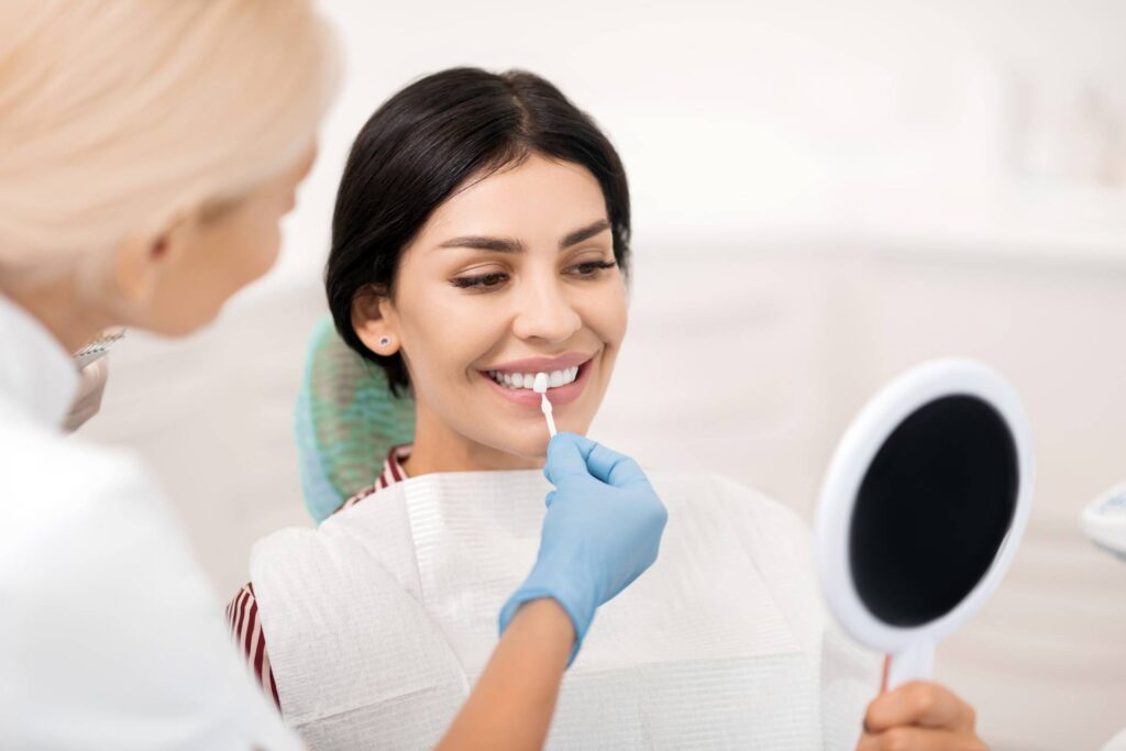 A dentist in a clinic helps a patient choose the dental veneers that best suit her in front of a mirror.