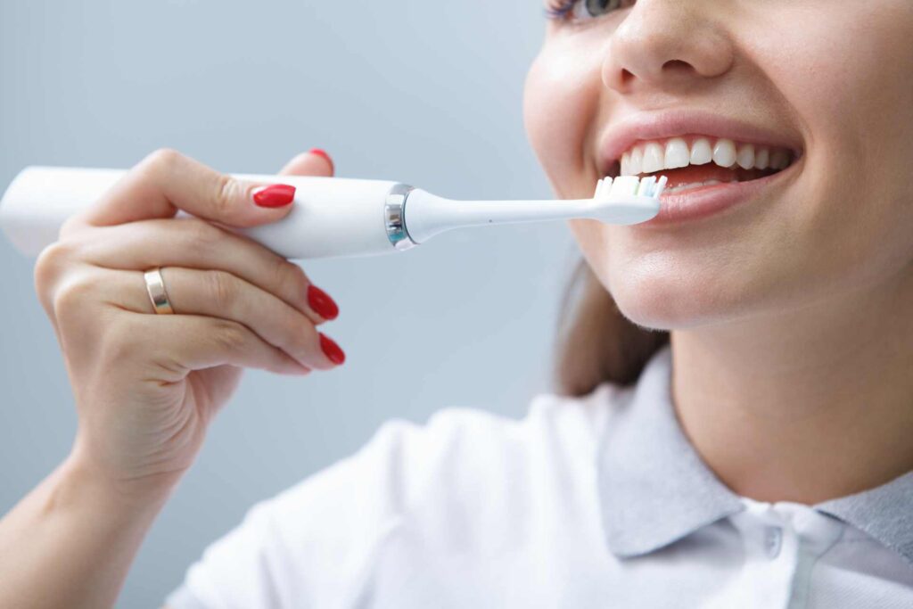 04 Young woman brushing with a soft-bristled electric toothbrush to prevent receding gums