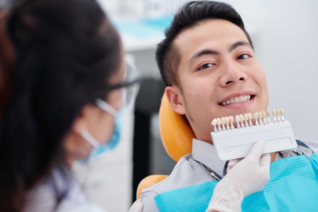 A dentist helps a patient choose from a porcelain veneer color chart.