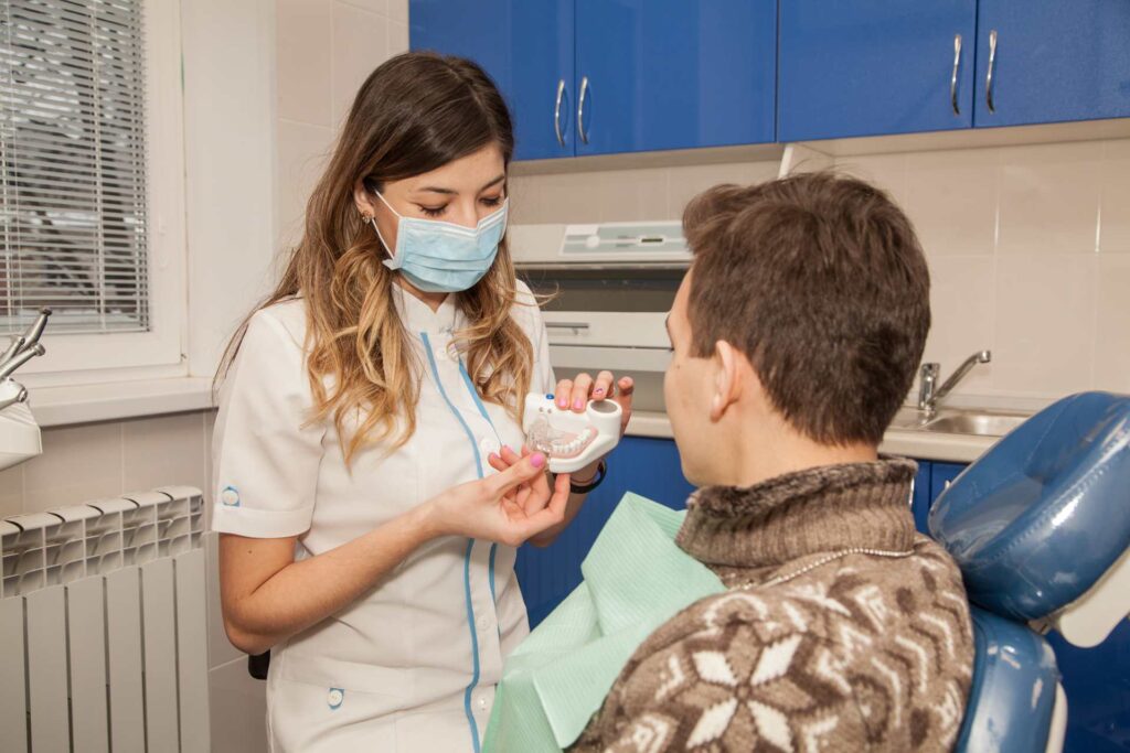 03 A dentist showing a human denture model to a patient_Porcelain veneers vs. bonding